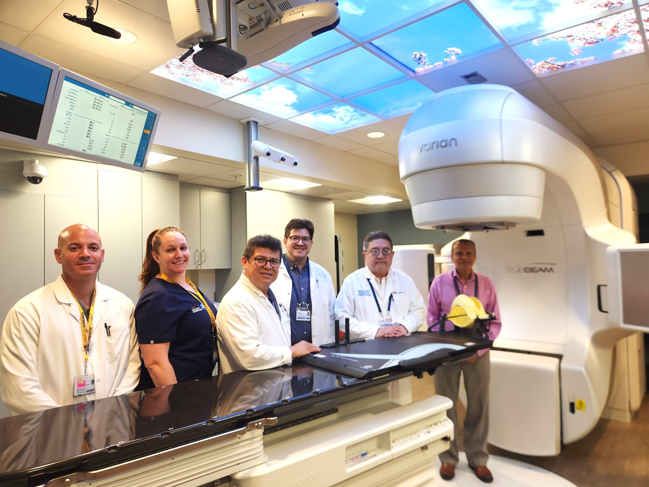 Members of the NYC Health + Hospitals/Queens Radiation Oncology team stand with the Varian TrueBeam linear accelerator, which was recently used to perform the hospital’s first successful Stereotactic Radiosurgery (SRS) procedure.