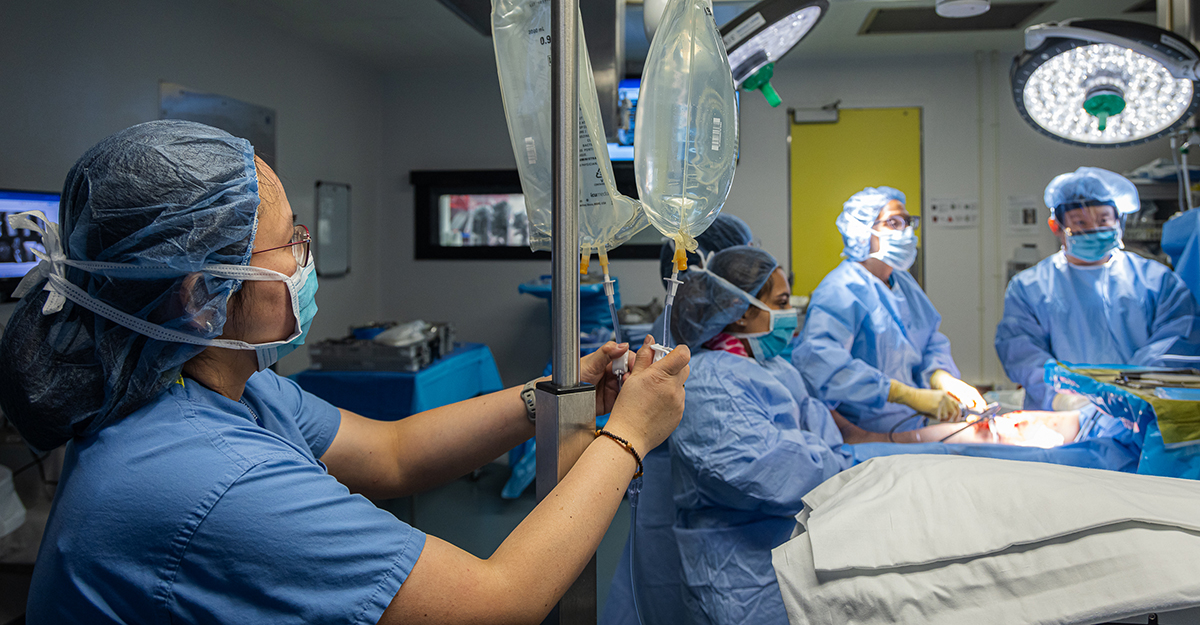 In the foreground, surgical RN Abigael Saavedra monitors the bags of a sterile solution of .9% sodium chloride, used to clear the surgical field to aid visualization in arthroscopic surgeries.