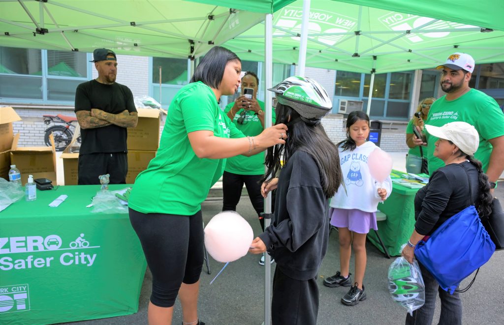 A Vision Zero representative helps a child try on a bicycle helmet during NYC Health + Hospitals/Metropolitan’s annual Back-to-School Fair, where families received school supplies, bicycle helmets and other resources for the new school year.