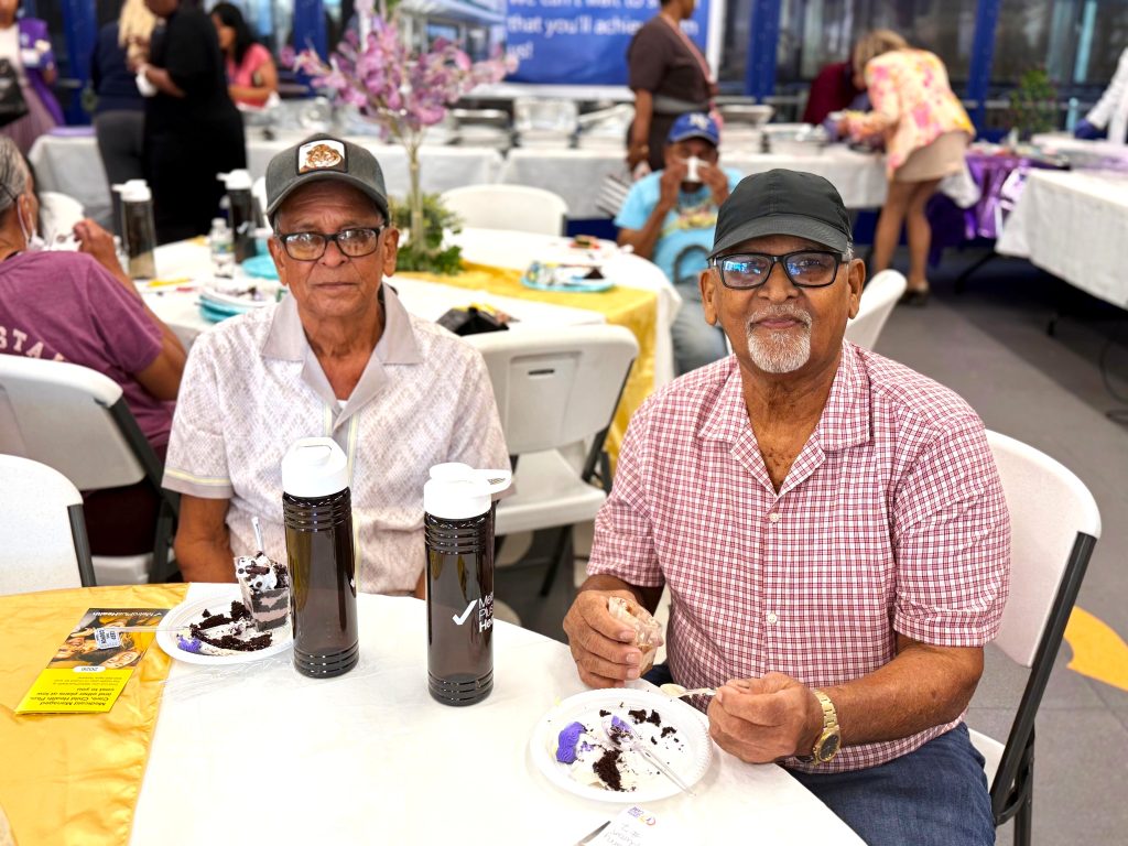 Two patients savor dessert together during the Annual Celebration of Life event at the Queens Cancer Center, enjoying a moment of joy and camaraderie as they celebrate their journeys of resilience and hope.