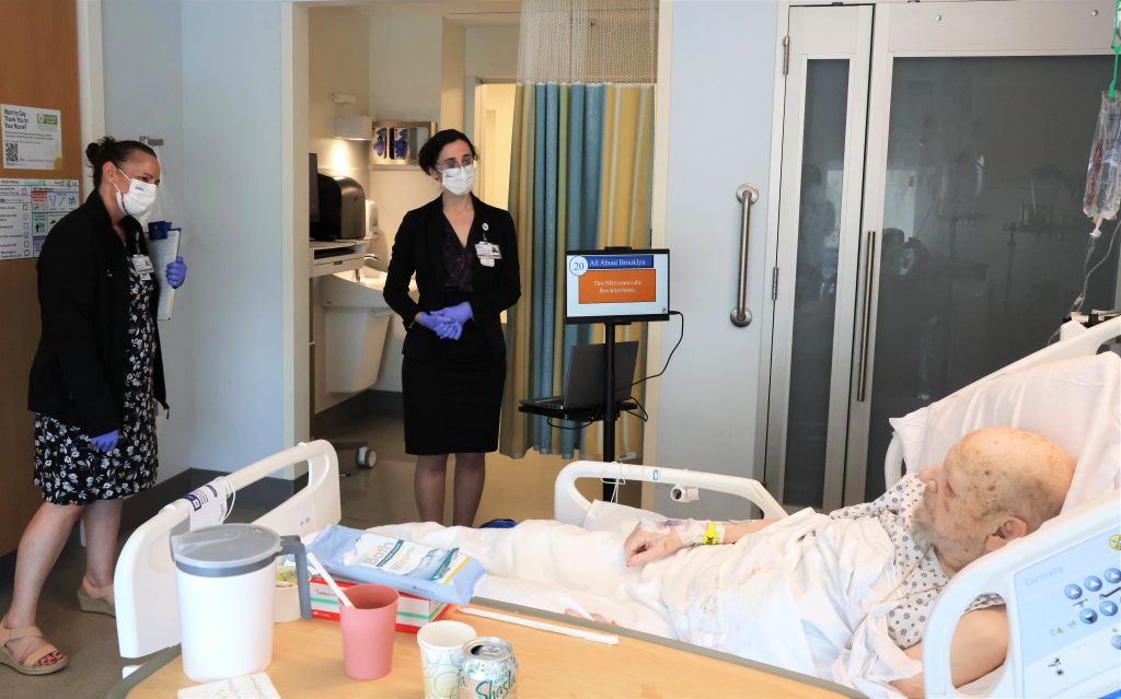 Julianne Rich, Director of Volunteer Services, and Riana Freedman, BRAVO Program Director, conduct a bedside visit with patient Leo Durocher.
