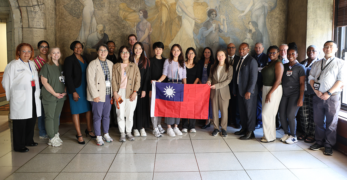 NYC Health + Hospitals/Kings County leadership with the National Taiwan University Hospital delegation in front of the historic Vincent Aderente mural in the hospital’s rotunda