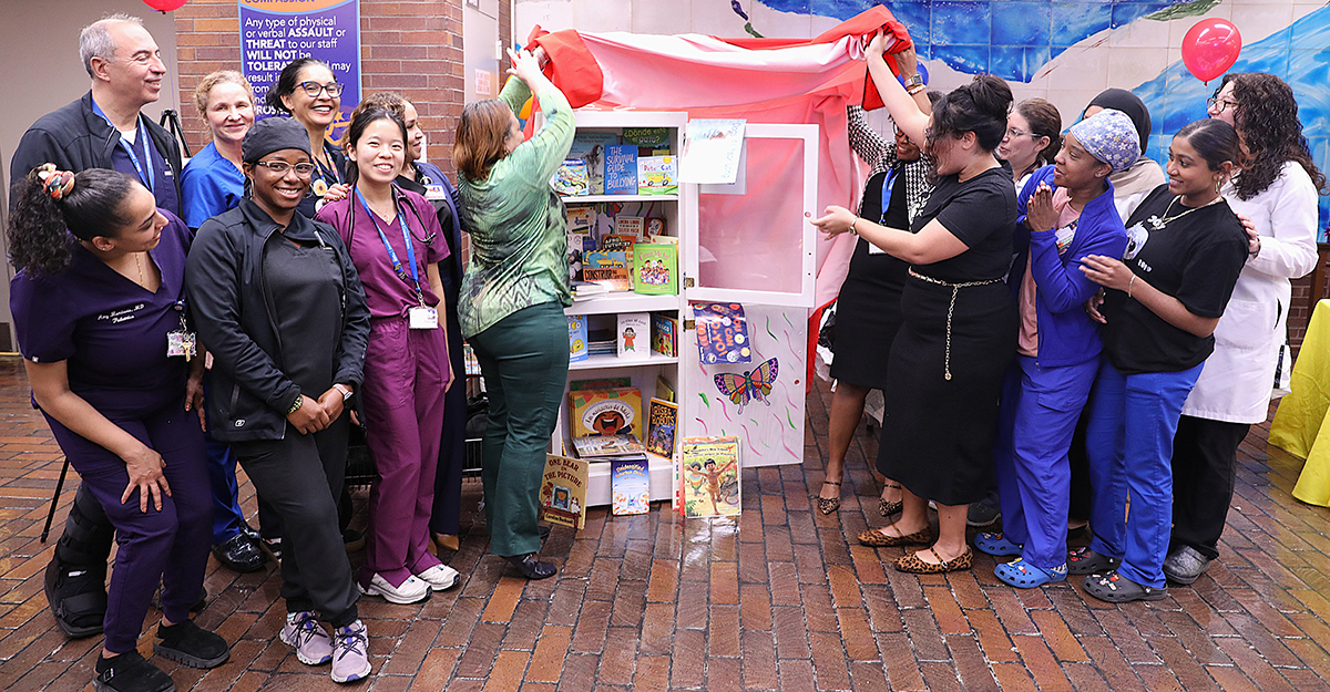 Pediatric staff with New York Public Library's Ruth Rodriguez (on the right in black) unveil the newly refurbished children's bookshelf.